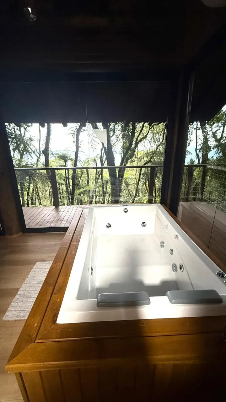 Banheira aquecida da Cabana Glass junto à parede de vidro, com a mata ao fundo