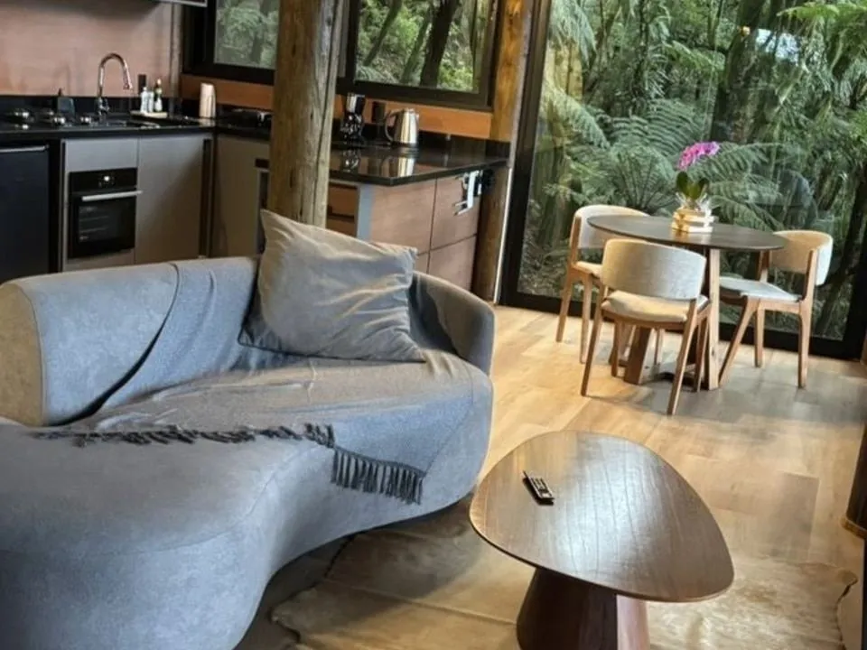 Sala da Cabana Glass com sofá curvo, cozinha e mesa voltadas para a mata