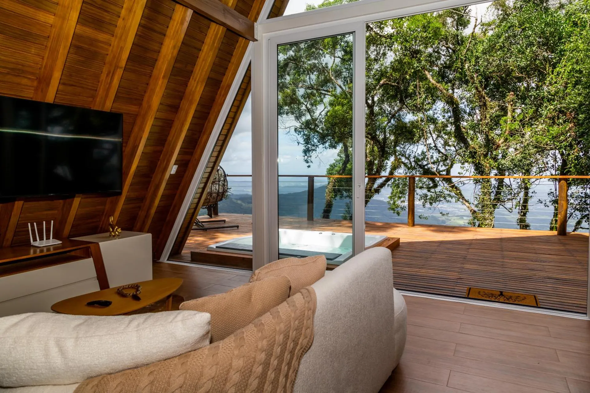 Sala com sofá curvo, TV e porta de vidro para a hidromassagem do deck